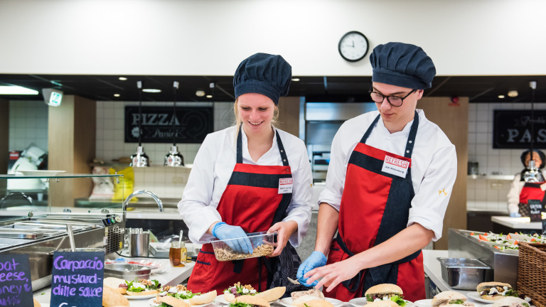 Twee studenten maken luxe broodjes gereed voor de lunch in het studentenrestaurant Refresh van Hotelschool Maastricht