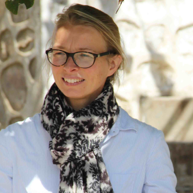 Maaike Kalse blond haar zwarte bril met een wit shirt en een sjaal om