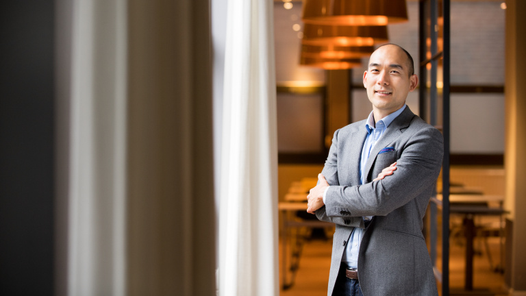 Danny Han staat voor het gastro lab met zijn handen over elkaar, draagt een grijs pak met blauw hemd