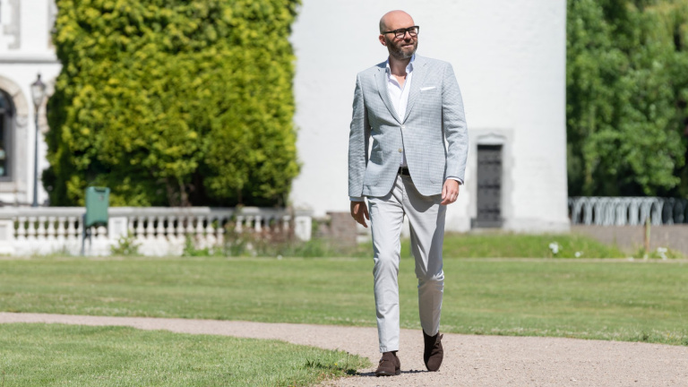 Bas Vogelsangs director of Hotel management school maastricht walking outside Teaching Hotel wearing a grey suit and black glasses